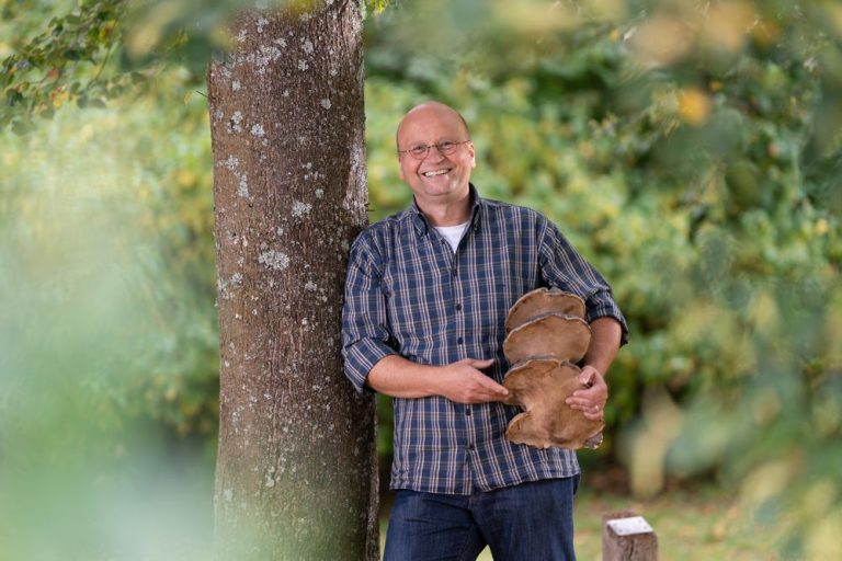 Volker Walther, Leiter des Pilzkundemuseums, fuehrt Gruppen durch das Museum und hilft den Gaesten bei der Bestimmung von Pilzen. Er lehnt mit einem Pilz unter dem Arm an einem Baum.     Mehr Infos: www.siegen-wittgenstein.info/s/IhUFO